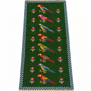 May include: A rectangular green needlepoint rug featuring a vertical column of eight colorful parrots perched on branches, flanked by small pink flowers. The rug has a blue and white geometric border and light-colored fringe on both ends.