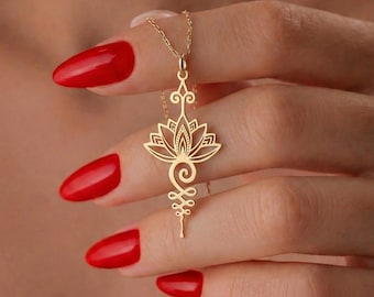 May include: A gold-colored necklace featuring a lotus flower pendant. The pendant has an intricate, openwork design with a spiral and a stylized symbol at the bottom. The necklace is displayed against a background of a person's hand with red nail polish.