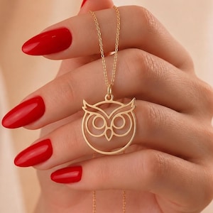 Può includere: Una collana color oro con un ciondolo circolare che presenta il design stilizzato e traforato di un volto di gufo. Il ciondolo è sospeso a una sottile e delicata catenina color oro, che mostra il profilo di un gufo con grandi occhi tondi.