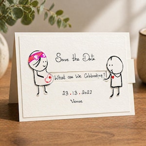 以下が含まれることがあります： 「Save the Date」の文字と「What are We Celebrating?」という質問が書かれた、手作りのオフホワイトのカード。2人の棒人間が描かれており、1人は妊娠しています。「23.13.2027」と「Venue」の日付もカードに書かれています。