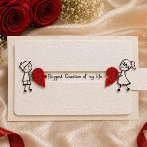May include: A cream-colored greeting card with the text "Biggest Question of my life." The card features stick figures holding red heart puzzle pieces. Red roses and a candle are in the background.