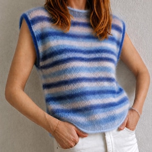 May include: A sleeveless knit sweater vest featuring a horizontal striped pattern in varying shades of blue, light blue, and white. The garment has a round neckline, wide armholes with ribbed trim, and a soft, fuzzy texture throughout the knit.