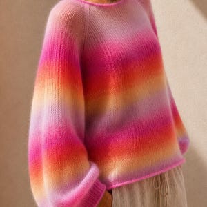 May include: A long-sleeved knit sweater featuring a vibrant gradient pattern that transitions through shades of pink, orange, and yellow. The garment has a round neckline, raglan sleeves, and ribbed cuffs, showcasing a soft, fuzzy texture throughout.