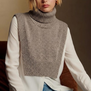 May include: A gray turtleneck knit collar worn over a white button-down shirt. The collar is a neutral color and has a ribbed texture. The turtleneck collar is a stylish accessory.