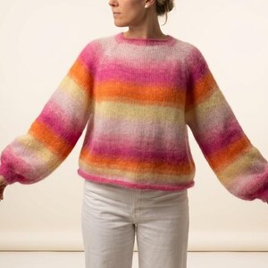 May include: A long-sleeved knit sweater featuring a horizontal striped pattern in vibrant shades of pink, orange, and pale yellow. The garment has a round neckline, a fuzzy texture, and loose-fitting sleeves that taper at the ribbed cuffs.
