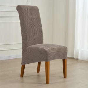 Può includere: Sedia da pranzo con una fodera color talpa con un motivo a linee curve ripetute. La sedia ha gambe in legno e si trova su uno sfondo neutro. La fodera offre uno strato decorativo e protettivo.