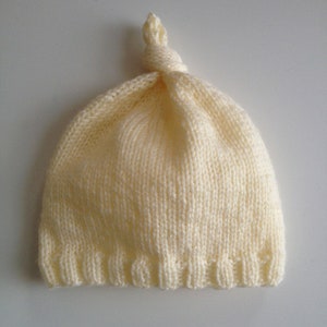 May include: A soft, cream-colored knitted baby hat with a knotted top.
