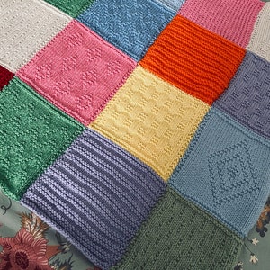 May include: A colorful patchwork blanket with various knitted patterns. The blanket features squares in shades of pink, blue, green, yellow, and orange. Each square has a unique texture, including diamond, striped, and floral designs.