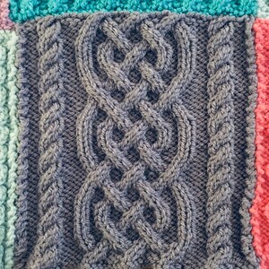 Peut inclure: Gros plan sur une couverture tricot&eacute;e avec un motif en c&acirc;ble gris. La couverture est compos&eacute;e de carr&eacute;s de diff&eacute;rentes couleurs, dont le bleu sarcelle, le rose et le bleu clair.