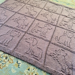 Könnte beinhalten: Eine mauvefarbene Strickdecke mit einem Gittermuster aus Quadraten, die jeweils die texturierte, erhabene Kontur eines Hundes enthalten. Die Decke ist in einer gleichmäßigen Rechts-Links-Stricktechnik gefertigt und erzeugt ein einheitliches, sich wiederholendes Hundemotiv.