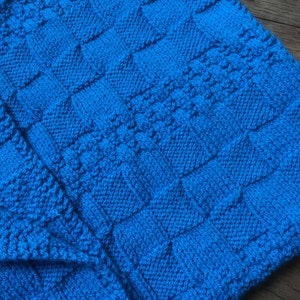 May include: A blue knitted blanket with a textured pattern. The blanket is made of soft yarn and has a cozy feel.