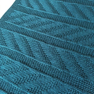 Puede incluir: Tejido de punto de color azul verdoso con un patrón geométrico de triángulos. El tejido es suave y texturizado.