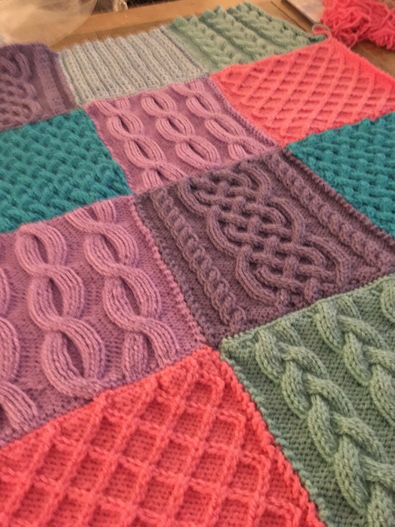 Peut inclure: Une couverture tricot&eacute;e color&eacute;e avec diff&eacute;rents motifs et textures. La couverture est faite de diff&eacute;rentes nuances de rose, violet, vert et bleu.