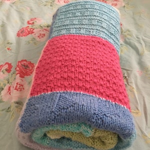 May include: A rolled up knitted baby blanket in shades of blue, pink, green, and white.