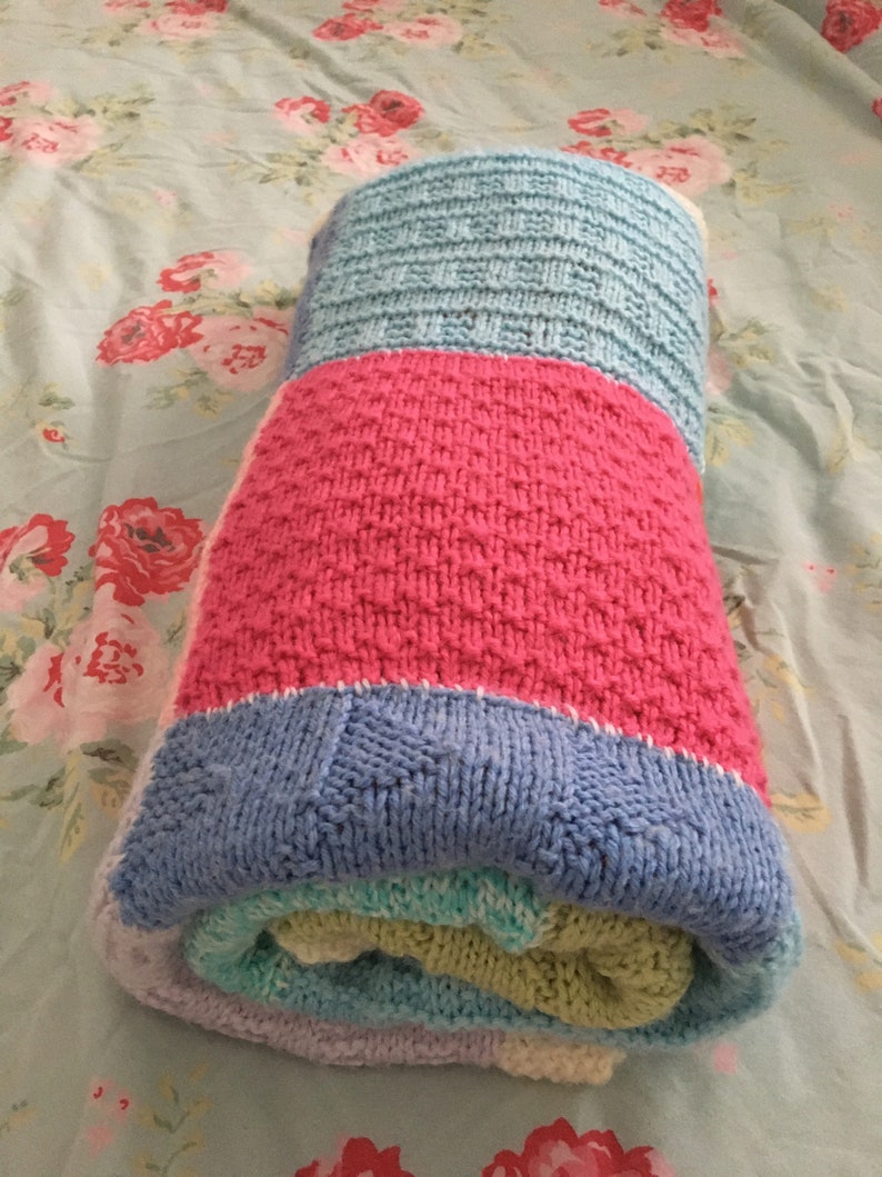 May include: A rolled up knitted baby blanket in shades of blue, pink, green, and white.