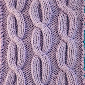 Peut inclure: Gros plan sur un tissu tricot&eacute; avec un motif de point de c&acirc;ble. Le tissu est de couleur violet clair.