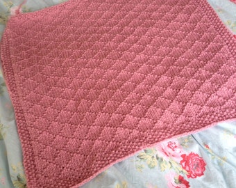 May include: A pink knitted baby blanket with a diamond pattern.