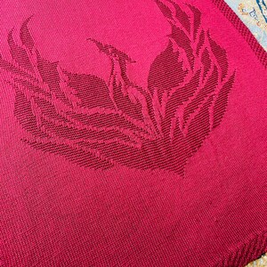 May include: A crimson red knitted blanket with a large, intricate design of stylized flames in the center.