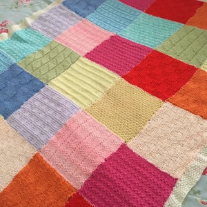 May include: A colourful knitted patchwork blanket with squares in various shades of blue, green, yellow, pink, orange and red.