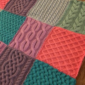 Peut inclure: Une couverture tricot&eacute;e avec un motif patchwork compos&eacute; de carr&eacute;s de diff&eacute;rentes couleurs et de diff&eacute;rents motifs de tricot. Les carr&eacute;s sont dans des tons de rose, violet, turquoise et gris.
