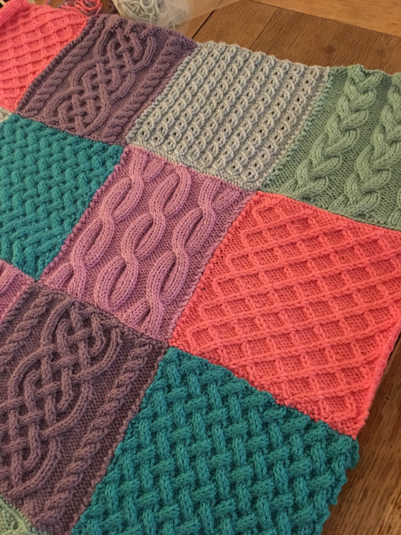Peut inclure: Une couverture tricot&eacute;e avec un motif patchwork compos&eacute; de carr&eacute;s de diff&eacute;rentes couleurs et de diff&eacute;rents motifs de tricot. Les carr&eacute;s sont dans des tons de rose, violet, turquoise et gris.
