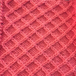 Peut inclure: Gros plan sur un tissu tricot&eacute; rose avec un motif en nid d'abeille.