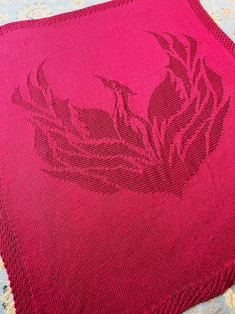 May include: A red knitted blanket with a large, detailed phoenix design in the center.