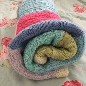 May include: A rolled up knitted blanket with stripes of light blue, pink, green, and purple.