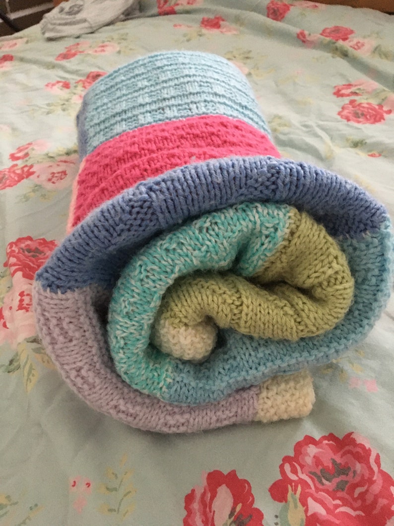 May include: A rolled up knitted blanket with stripes of light blue, pink, green, and purple.