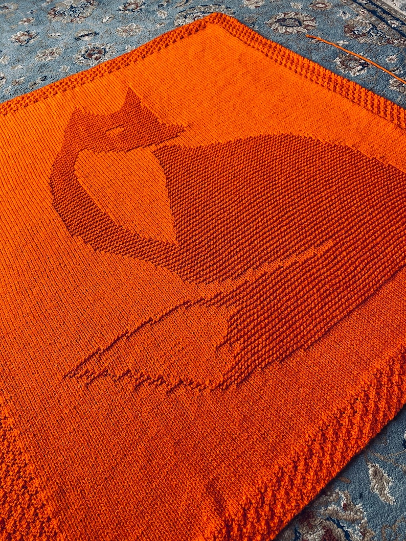 May include: A large orange knitted blanket with a cat silhouette design.