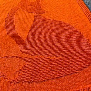 May include: Orange knitted blanket with a cat silhouette design.