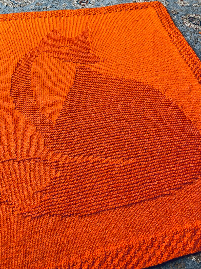 May include: Orange knitted blanket with a cat silhouette design.