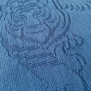 Pode incluir: Um close-up de um cobertor de malha azul com um padr&atilde;o texturizado. O padr&atilde;o &eacute; um desenho repetitivo de pequenos quadrados e ret&acirc;ngulos.