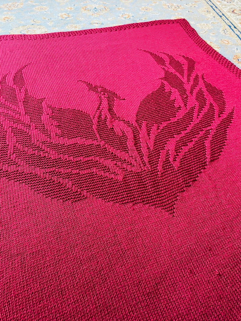 May include: A red knitted blanket with a large, stylized phoenix design in the center.