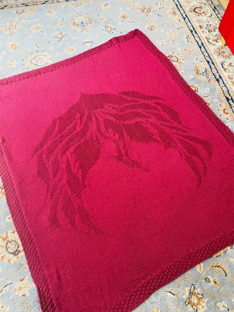 May include: A burgundy knitted throw blanket with a large, embroidered wing design.