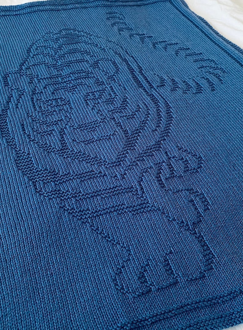 Pode incluir: Uma manta de tric&ocirc; azul com um grande desenho intrincado de um p&aacute;ssaro no centro.