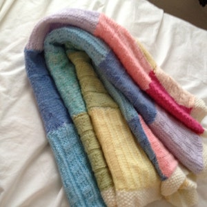 May include: A multi-colored knitted blanket with stripes of lavender, pink, yellow, green, and blue.