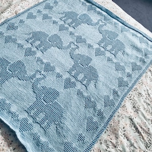 Könnte beinhalten: Eine hellblaue gestrickte Babydecke mit einem Muster aus Elefanten und Herzen.