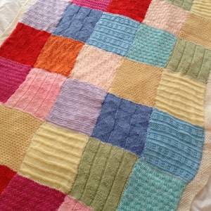 May include: A knitted patchwork blanket with squares in various colors, including pink, blue, green, yellow, and purple. The blanket is made of different textures and patterns.