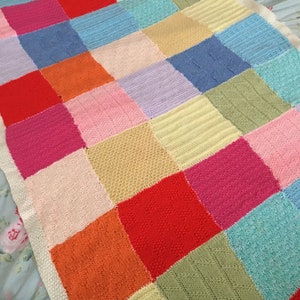 May include: A colorful knitted blanket with a patchwork design. The squares are in various colors, including pink, red, orange, yellow, green, blue, and purple.