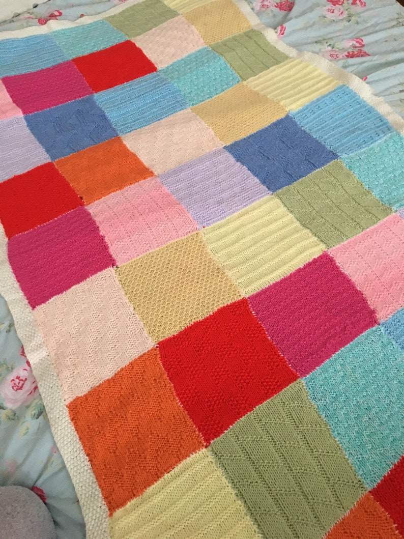 May include: A colorful knitted blanket with a patchwork design. The squares are in various colors, including pink, red, orange, yellow, green, blue, and purple.