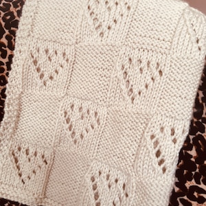May include: A cream-coloured knitted blanket with a lacy pattern. The blanket is made of soft yarn and has a delicate, feminine feel.