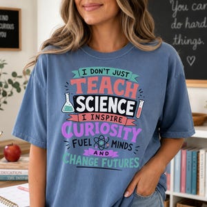 May include: A blue short-sleeve t-shirt featuring the text I DON'T JUST TEACH SCIENCE I INSPIRE CURIOSITY FUEL MINDS AND CHANGE FUTURES. The graphic includes illustrations of a beaker, a test tube, and an atom symbol in pink, white, and teal.