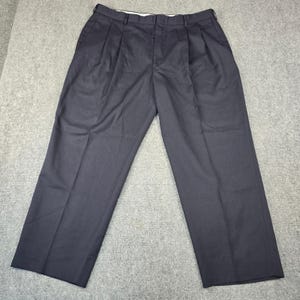 May include: A pair of dark navy blue trousers featuring a pleated front design, a waistband with belt loops, and a button and zipper fly closure. The pants have a straight leg cut and a smooth, solid-colored fabric finish throughout the garment.