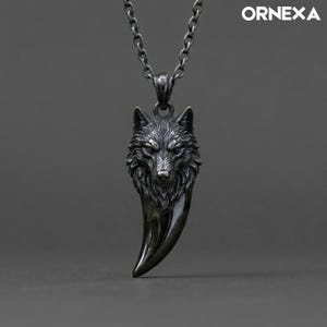 Puede incluir: Un collar de metal gris oscuro con un colgante de cabeza de lobo detallada que se transforma en una forma curva y lisa similar a un colmillo. El colgante cuelga de una cadena de metal a juego. El texto ORNEXA es visible en la esquina superior derecha.