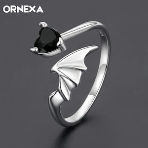 May include: A silver open-style ring featuring a black heart-shaped gemstone at one end and a bat wing design at the other. The band is polished silver with the text ORNEXA visible in the upper left corner and S925 stamped on the inner band.