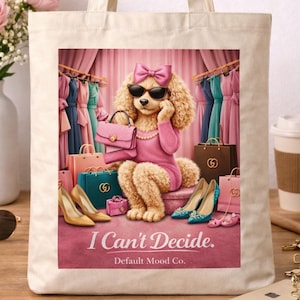 May include: Cream-colored tote bag featuring a cartoon poodle wearing sunglasses and a pink dress, surrounded by shopping bags and shoes. The text "I Can't Decide" is displayed on the bag.