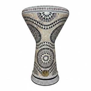 May include: A decorative, handcrafted darbuka drum. The drum features a beige body with intricate black and white geometric patterns. The top rim has a series of small, dark red accents. A small, gold-colored emblem is near the base.