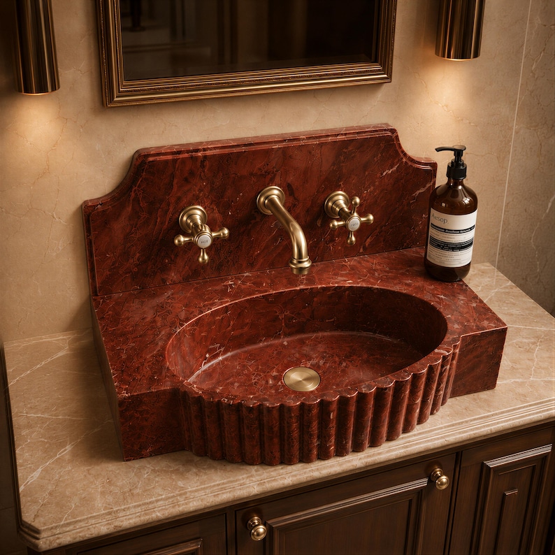 a bathroom sink with a red marble basin, a gold faucet, and a soap dispenser on the countertop.