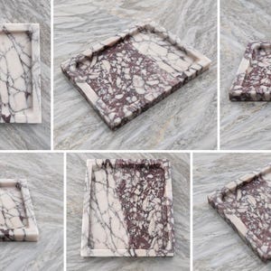 May include: A rectangular marble tray featuring a distinct brecciated pattern with deep burgundy and white veining. The tray has a smooth, polished surface and raised edges, showcasing a natural stone texture with a high-contrast color palette.